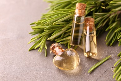 Photo of Essential oil in bottles and rosemary on grey table