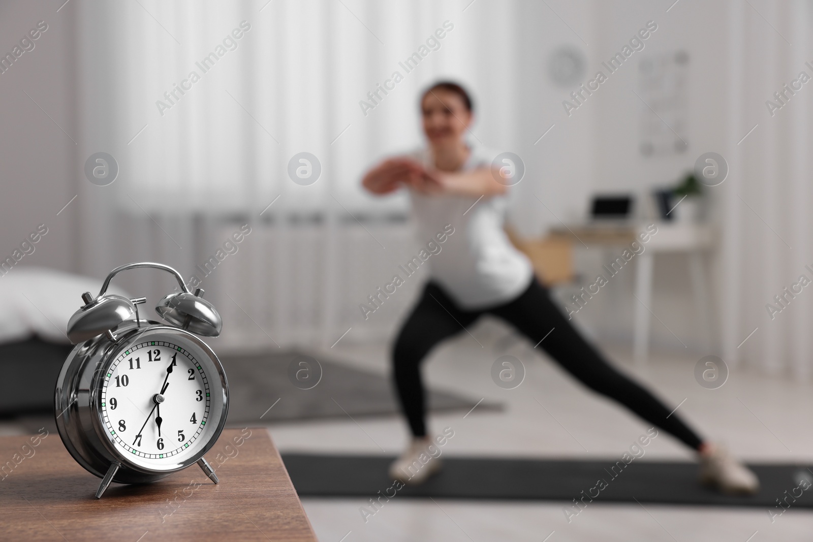 Photo of Morning routine. Alarm clock on wooden table and woman doing exercise, selective focus. Space for text