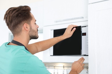 Photo of Young man using modern microwave oven at home