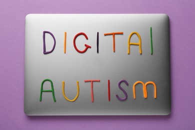 Photo of Phrase Digital Autism made of colorful plasticine with laptop on purple background, top view