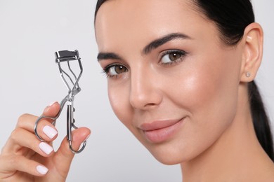 Beautiful young woman with eyelash curler on white background, closeup