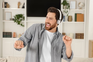 Photo of Emotional man dancing while listening music with headphones at home