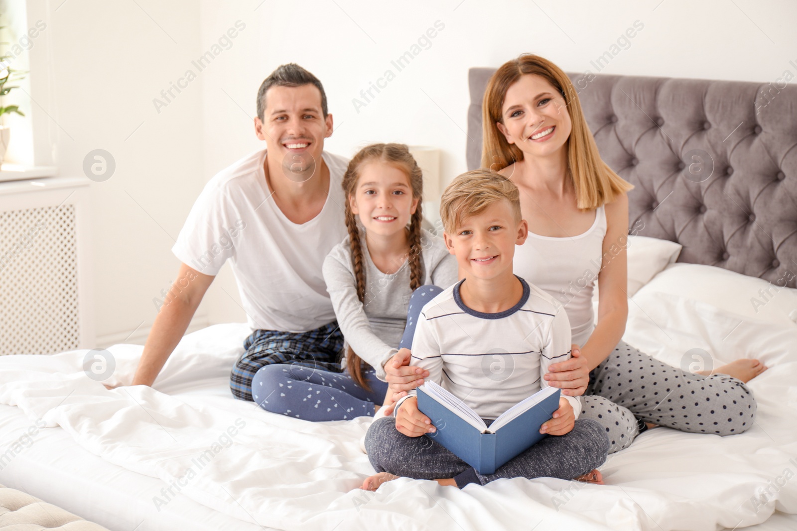 Photo of Child reading book to family in bedroom. Spending time together