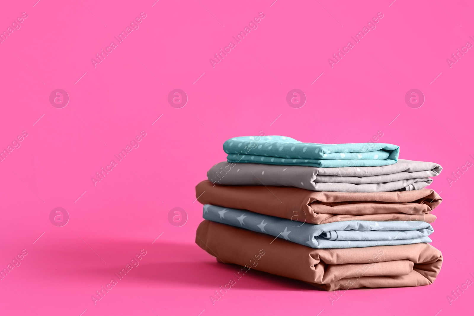 Photo of Stack of clean bed sheets on pink background. Space for text