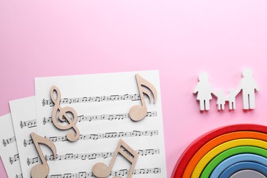 Photo of Baby songs. Music sheets, figures of family, wooden notes and toy rainbow on pink background, flat lay