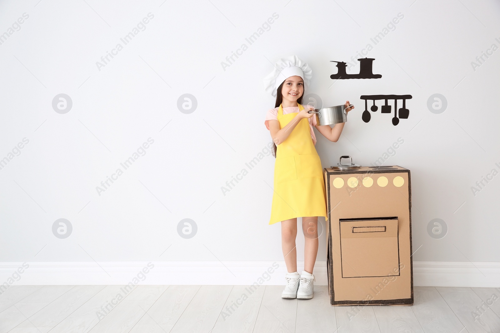 Photo of Little child in chef hat playing with carton stove indoors