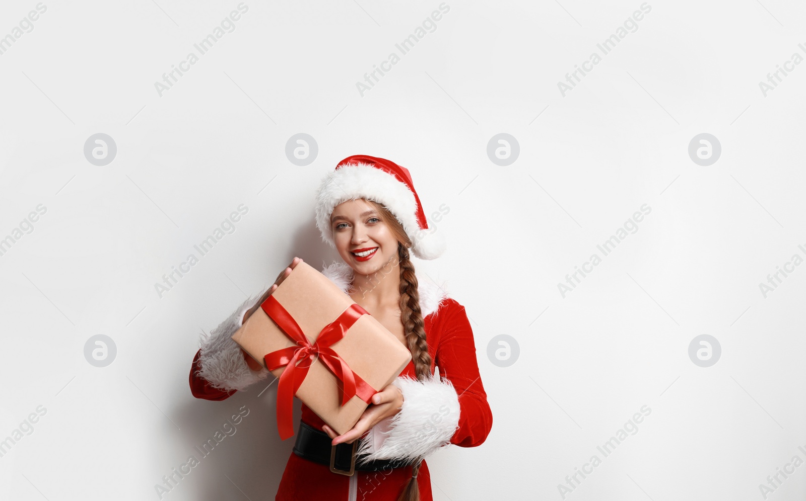 Photo of Beautiful Santa girl with Christmas gift on light background. Space for text