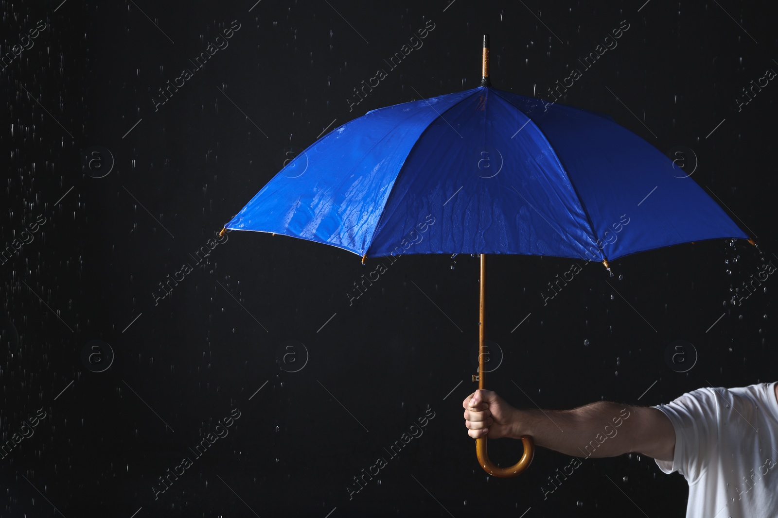 Photo of Man holding blue umbrella under rain against black background, closeup