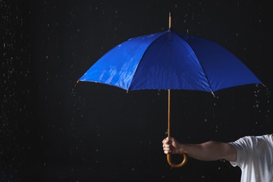 Photo of Man holding blue umbrella under rain against black background, closeup