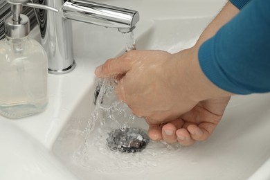 Photo of Man using water tap to wash hands in bathroom, closeup