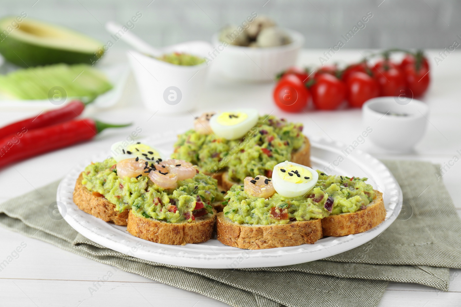 Photo of Slices of bread with tasty guacamole, eggs and shrimp on white wooden table, closeup