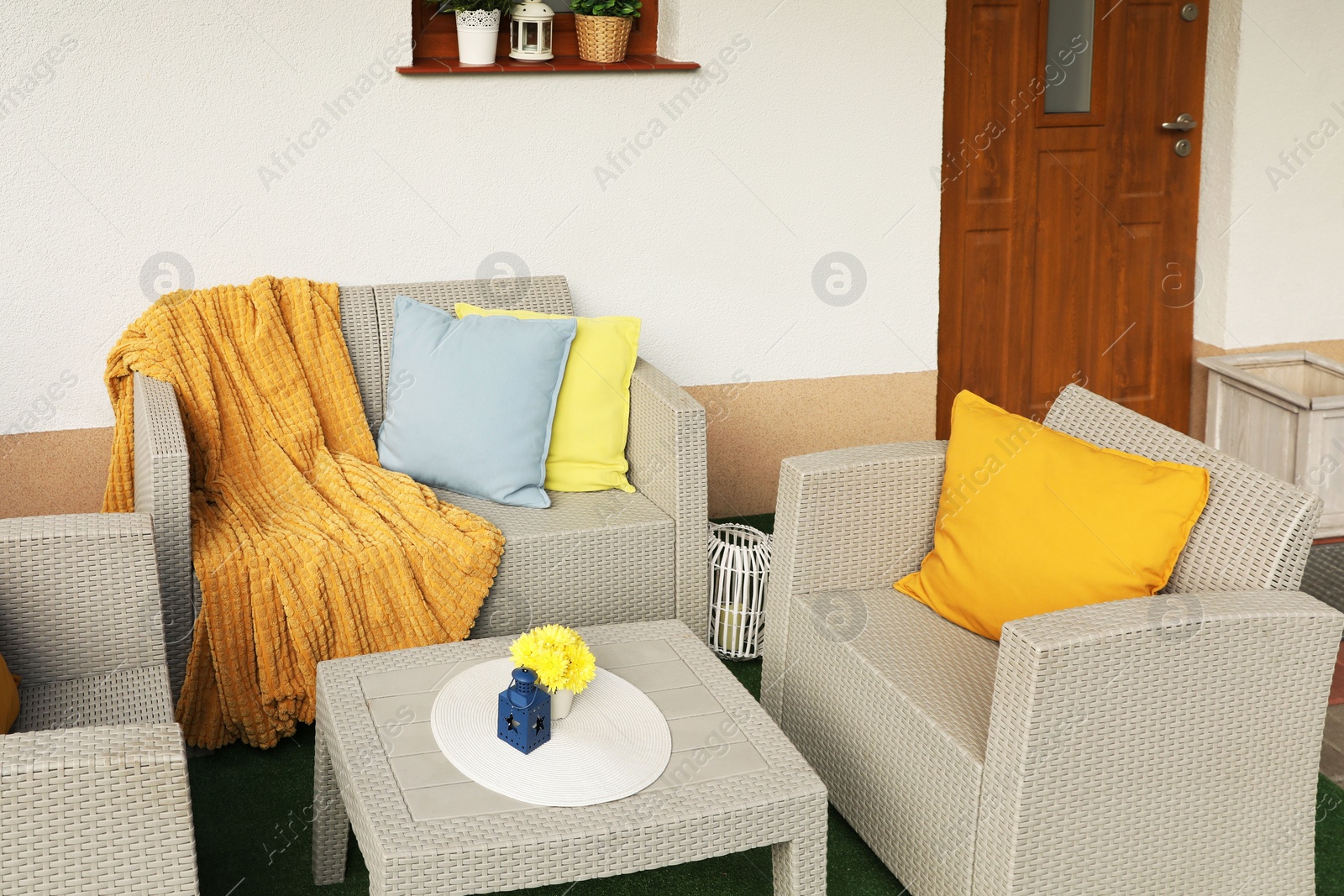 Photo of Beautiful rattan garden furniture, soft pillows, blanket and yellow chrysanthemum flowers outdoors