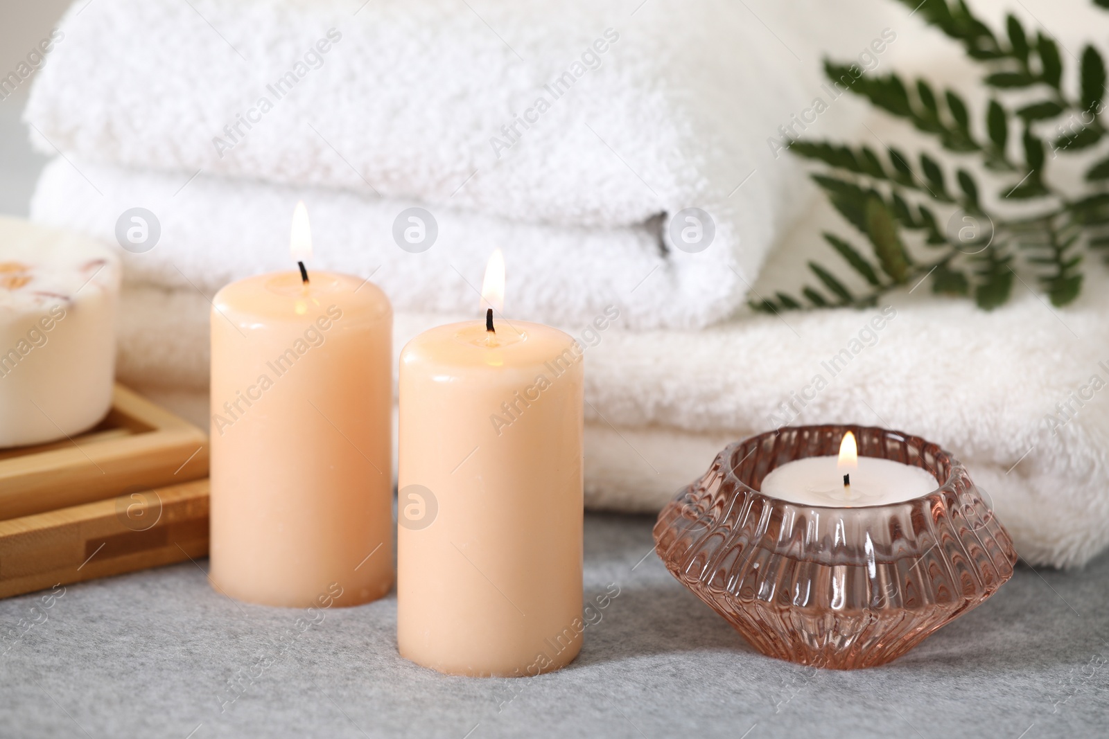 Photo of Spa composition. Burning candles and towels on soft grey surface