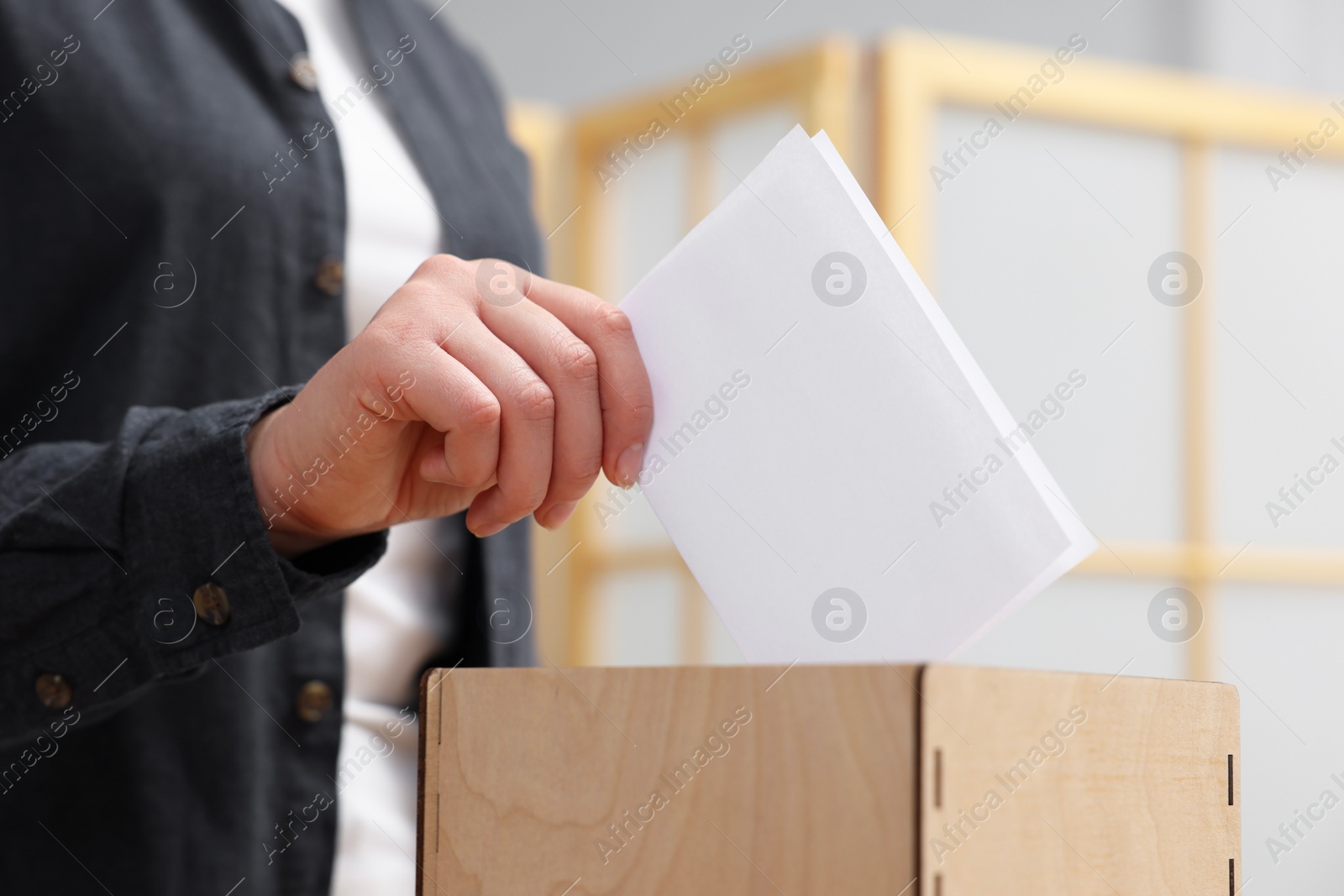 Photo of Woman putting her vote into ballot box on blurred background, closeup