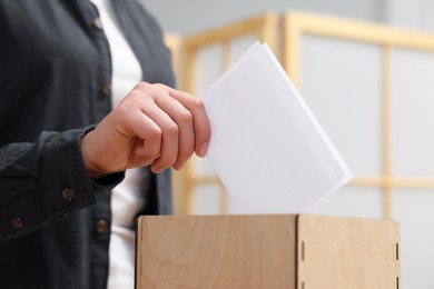 Photo of Woman putting her vote into ballot box on blurred background, closeup