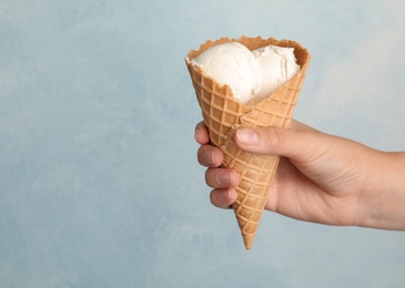 Photo of Woman holding delicious ice cream in wafer cone on light blue background, closeup. Space for text