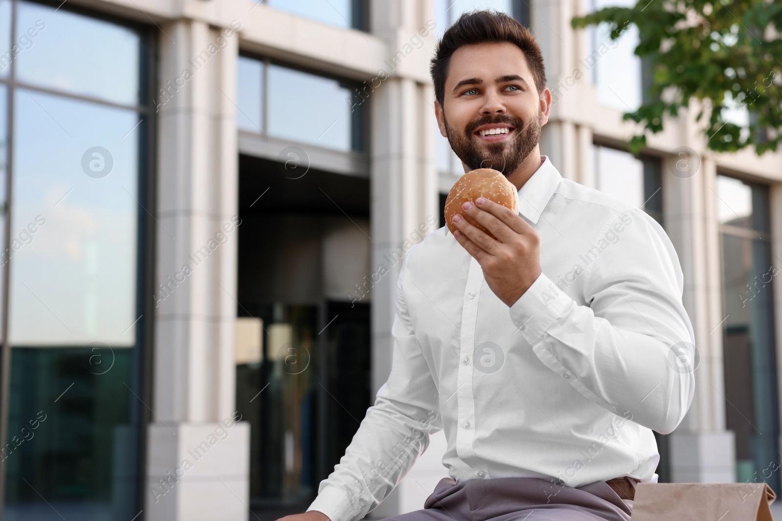 Photo of Happy businessman with hamburger having lunch outdoors