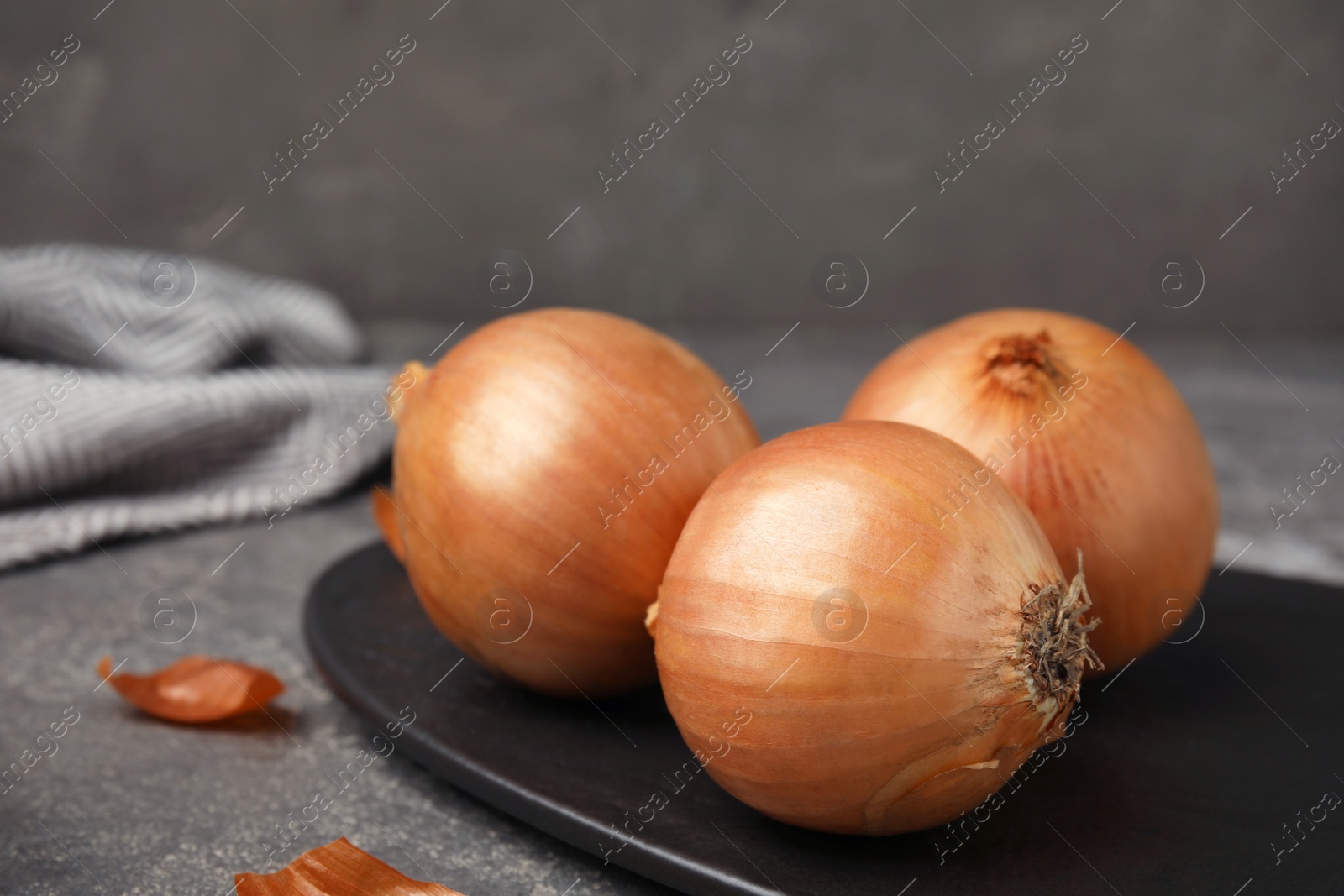 Photo of Slate plate with ripe onions on grey table, space for text