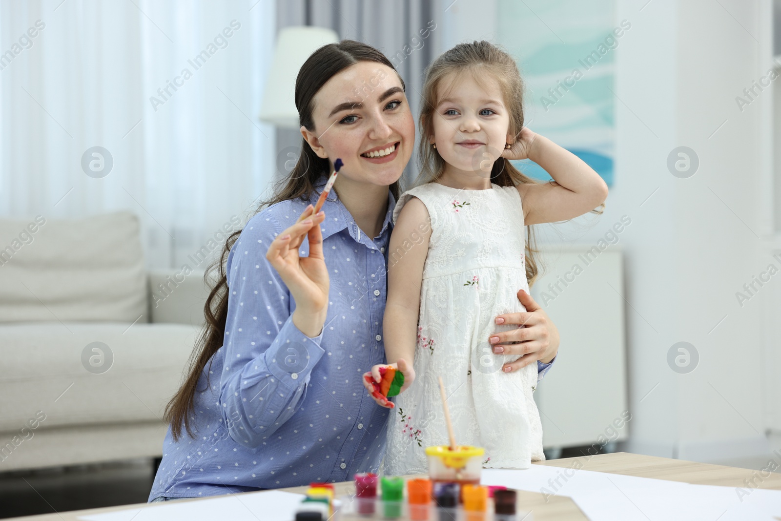 Photo of Mother and her little daughter painting with palms at home