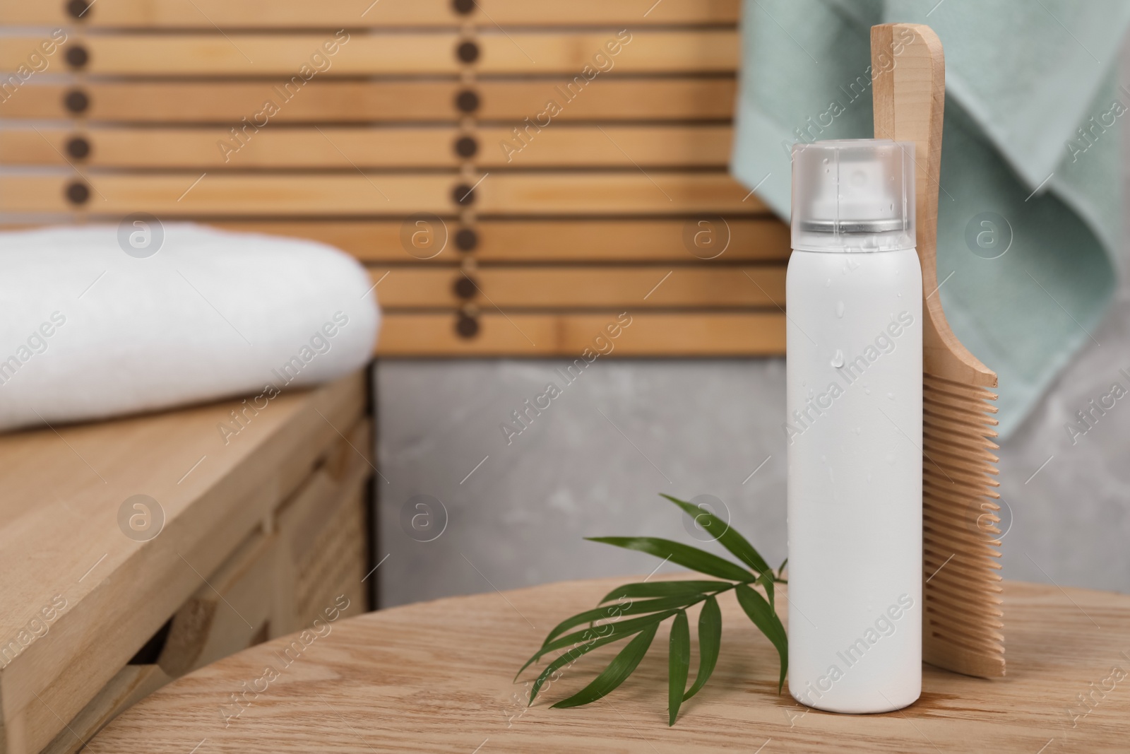 Photo of Dry shampoo spray, green leaves and comb on wooden table in bathroom. Space for text