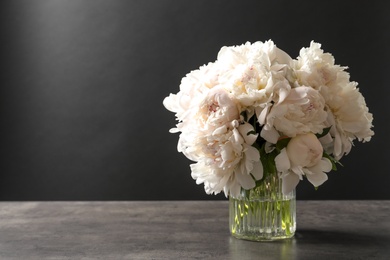 Photo of Vase with beautiful blooming peonies on table against black background