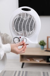 Photo of Woman turning on electric fan heater at home, closeup