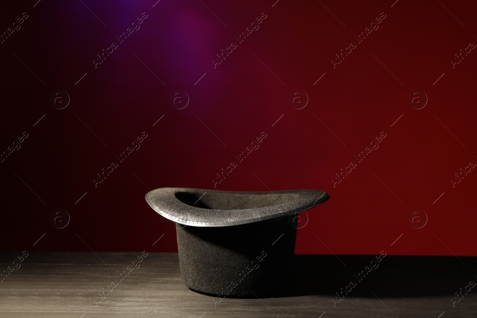 Photo of Magician's hat on black wooden table against color background, space for text