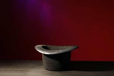 Photo of Magician's hat on black wooden table against color background, space for text