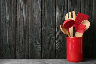 Photo of Holder with kitchen utensils on grey table against dark wooden background. Space for text