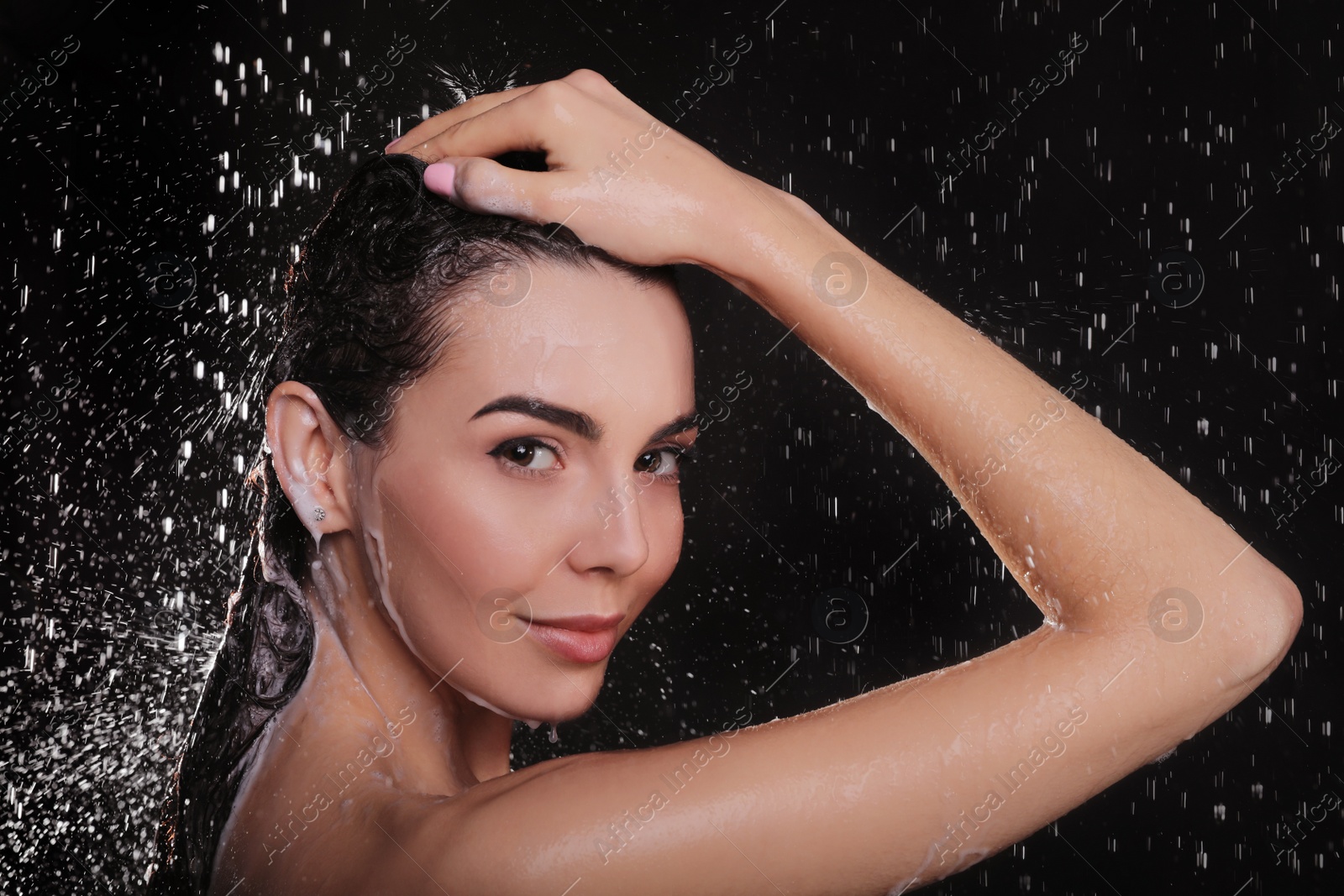 Photo of Young woman washing hair while taking shower on black background