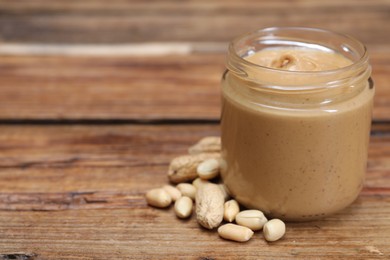 Tasty nut paste in jar and peanuts on wooden table, closeup. Space for text