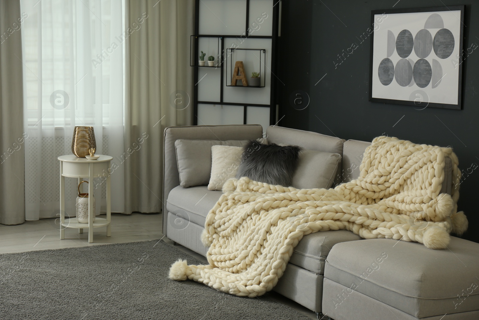 Photo of Comfortable sofa with knitted plaid in living room. Interior design