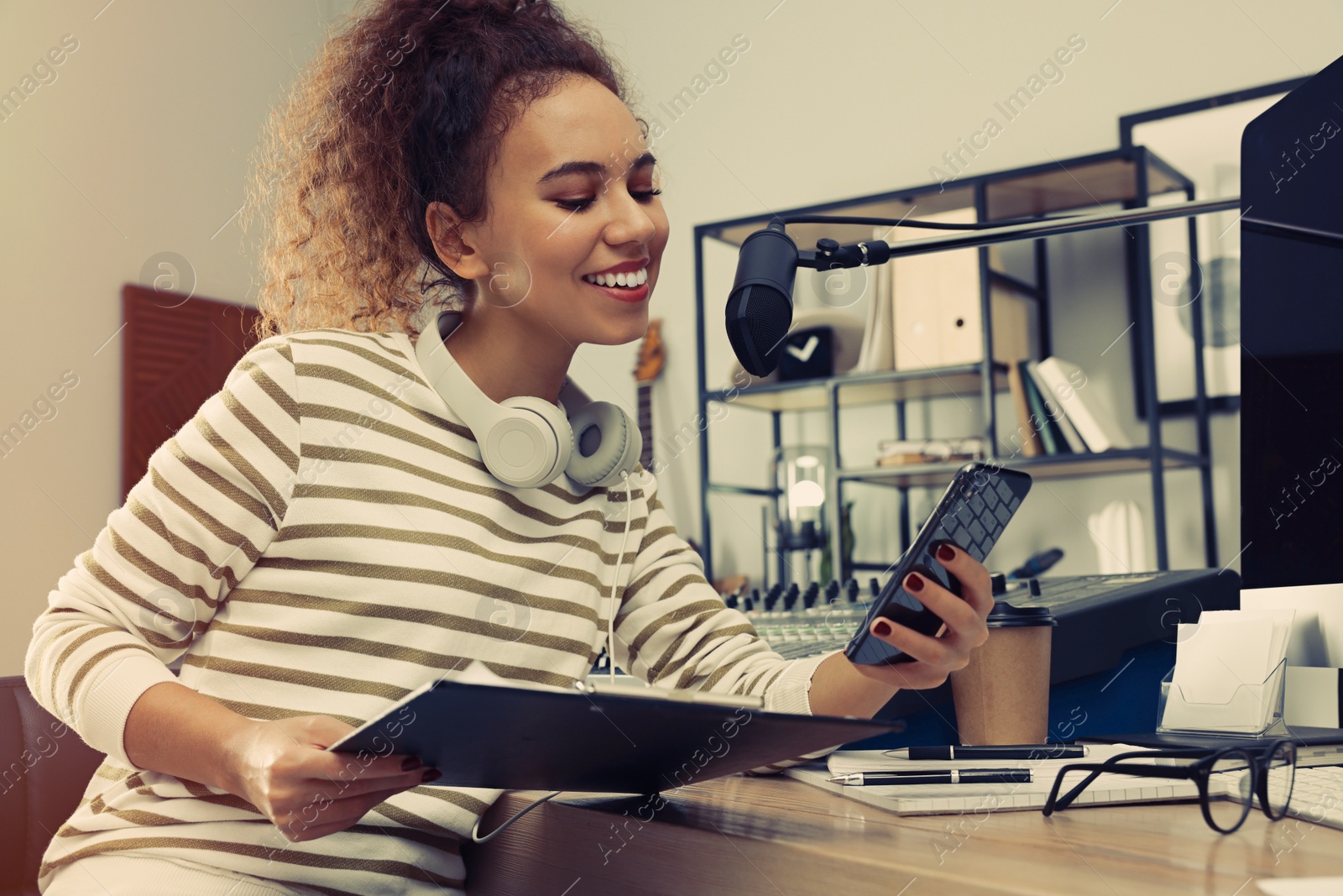 Photo of African American woman with smartphone working as radio host in modern studio