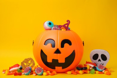 Halloween trick or treat bucket with different sweets on yellow background