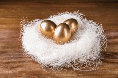 Photo of Golden eggs in nest on wooden table. Pension planning