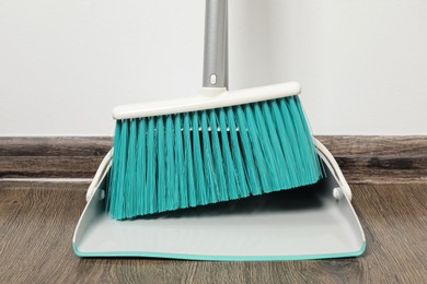 Photo of Plastic broom with dustpan near light wall indoors, closeup