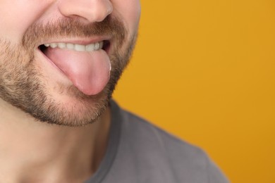 Photo of Man showing his tongue on yellow background, closeup. Space for text