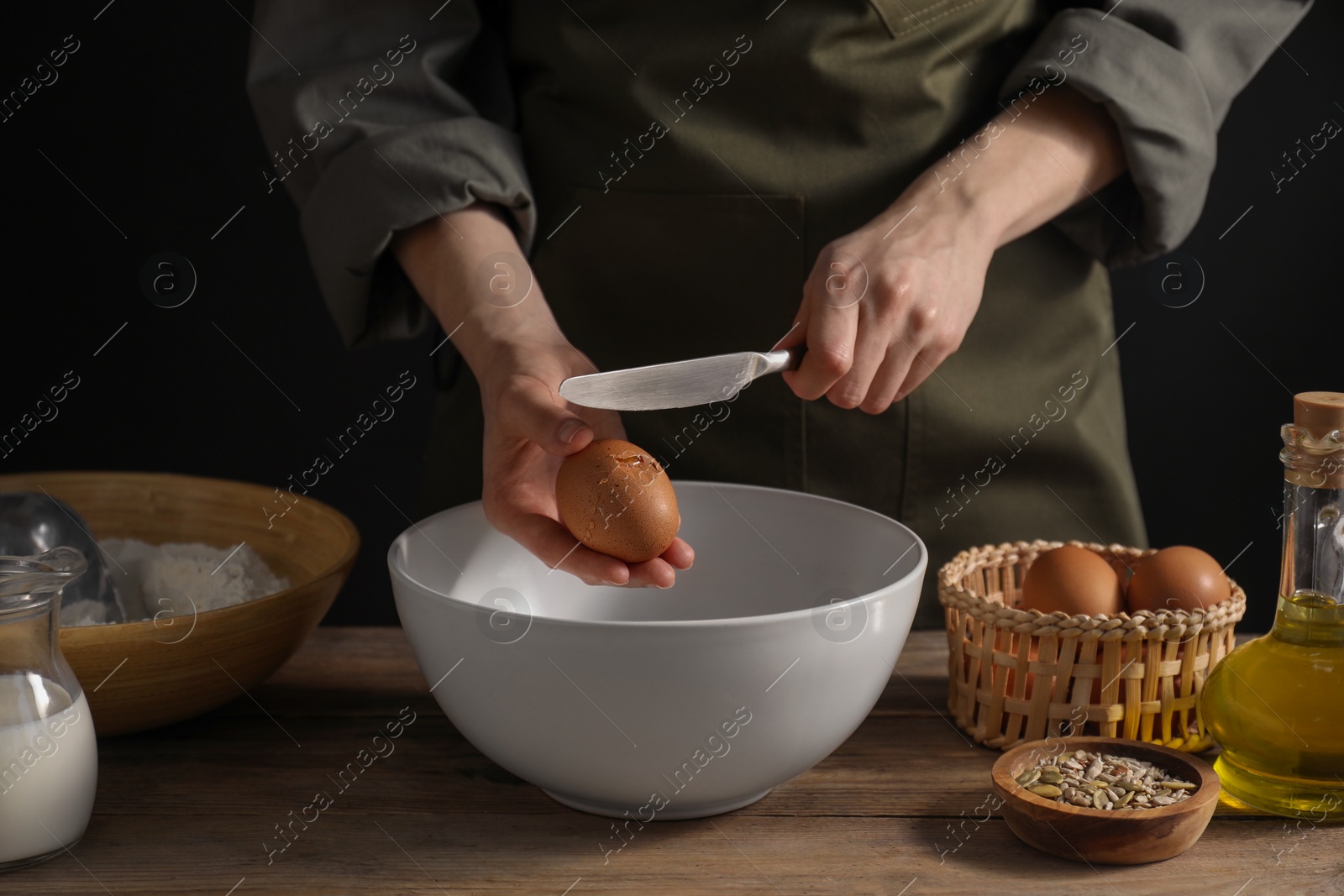 Photo of Making bread. Woman adding egg into dough at wooden table on dark background, closeup