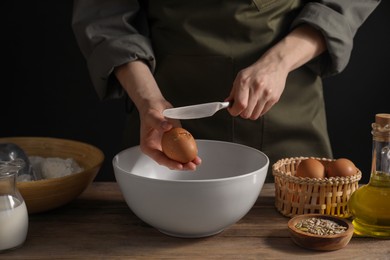 Making bread. Woman adding egg into dough at wooden table on dark background, closeup