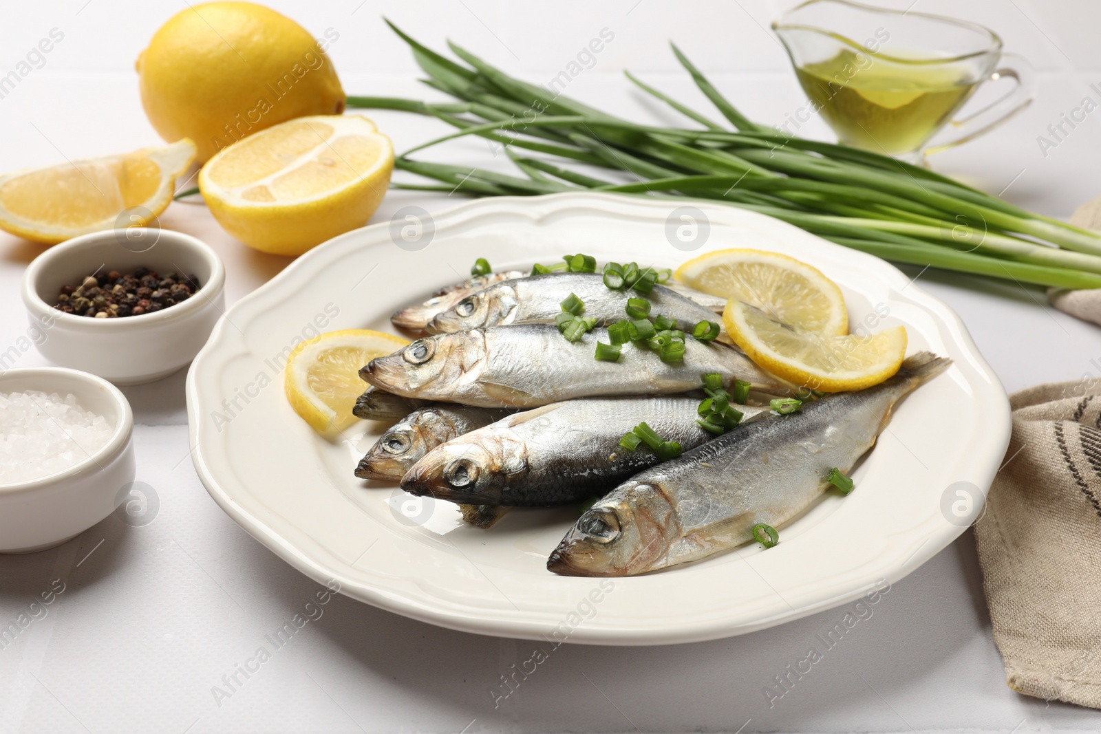 Photo of Fresh raw sprats, green onion, spices and cut lemon on white table, closeup