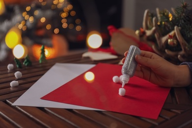 Little child making Christmas card at wooden table, closeup