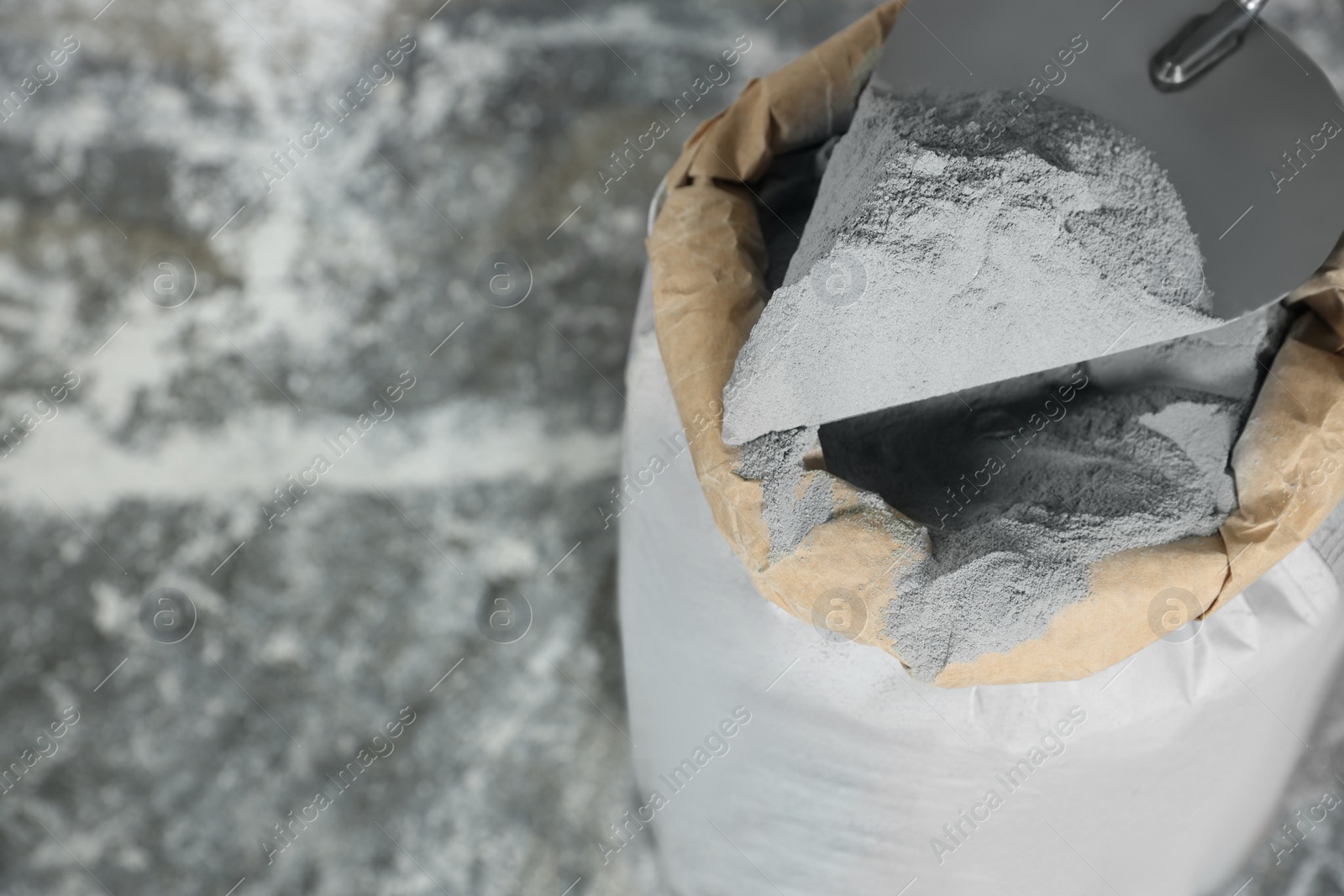 Photo of Cement powder and trowel put in bag on stone floor, above view. Space for text