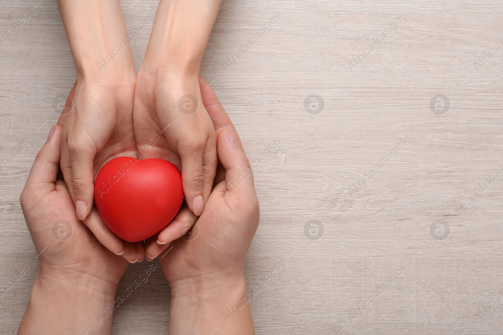 Photo of People holding red decorative heart on wooden background, top view and space for text. Cardiology concept