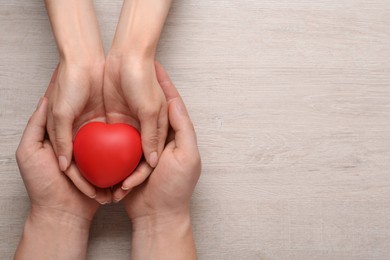 Photo of People holding red decorative heart on wooden background, top view and space for text. Cardiology concept