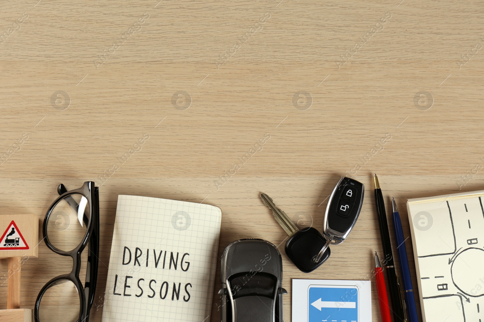 Photo of Flat lay composition with driving lessons workbook and toy car on wooden background, space for text. Passing license exam