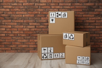 Photo of Cardboard boxes with different packaging symbols on floor near brick wall. Parcel delivery