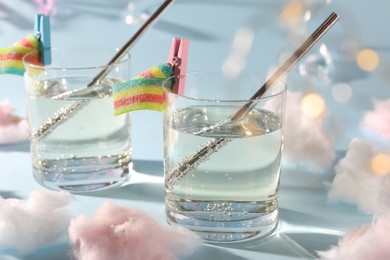 Tasty cocktails in glasses decorated with gummy candies and cotton candy on light blue background, closeup