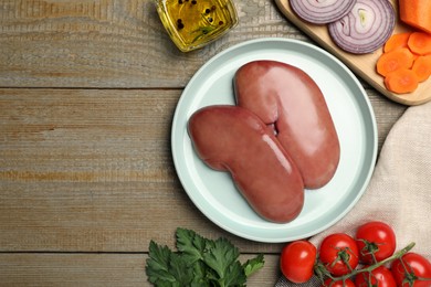 Photo of Plate with fresh raw pork kidneys and different products on wooden table, flat lay. Space for text