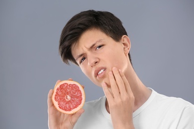 Teenage boy with acne problem holding grapefruit on grey background. Skin allergy