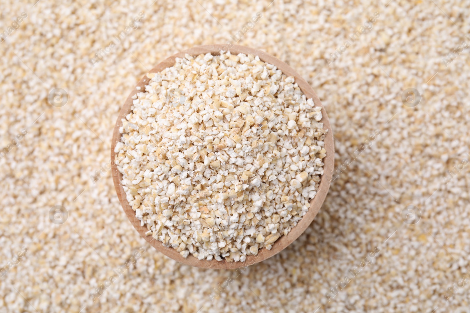 Photo of Wooden bowl on raw barley groats, top view